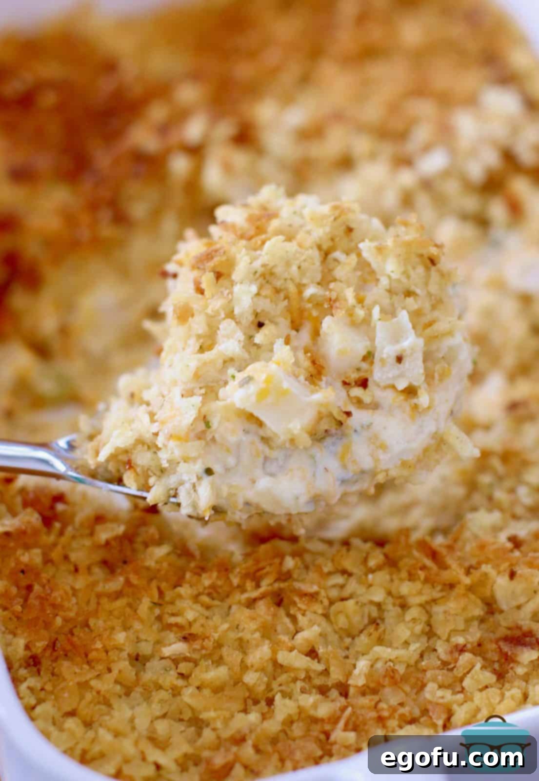 A large silver spoon scooping up Funeral Potatoes out of a casserole dish, highlighting the creamy interior and crunchy topping.