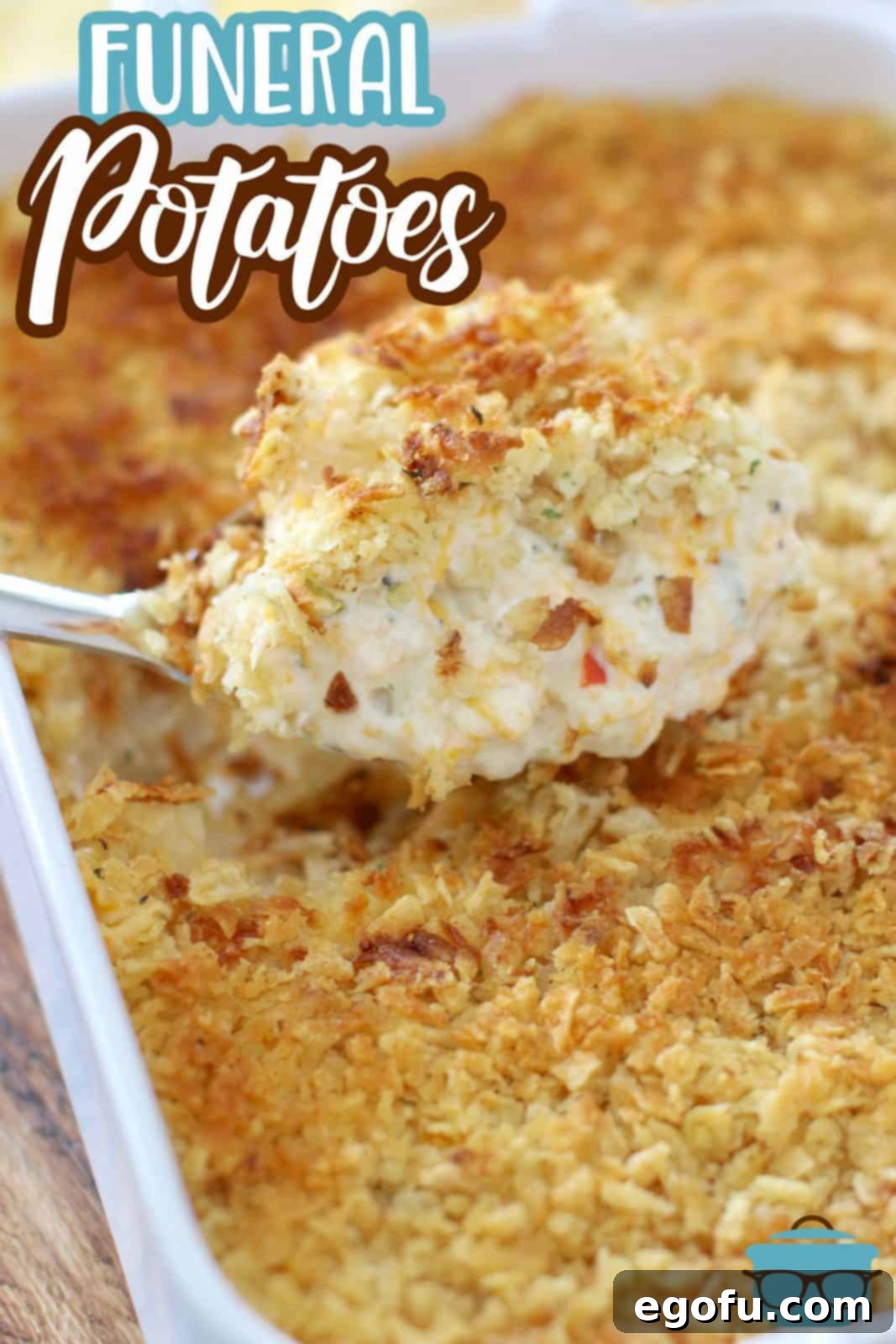 Funeral Potatoes recipe from The Country Cook. A large silver spoon showing a generous scoop of funeral potatoes being removed from a white casserole dish, showcasing the creamy filling and golden topping.