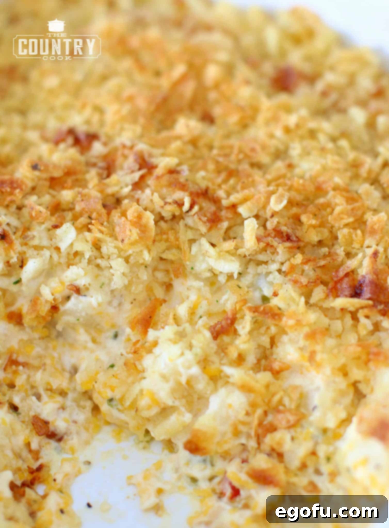 Fully baked Funeral Potatoes in a casserole dish, with a serving removed to show the creamy, cheesy interior and crunchy topping.