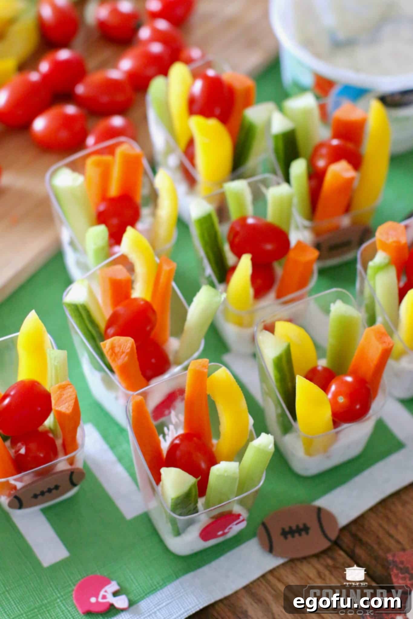 Individual veggie dip cups on a football patterned tablecloth, ready for a game day party.