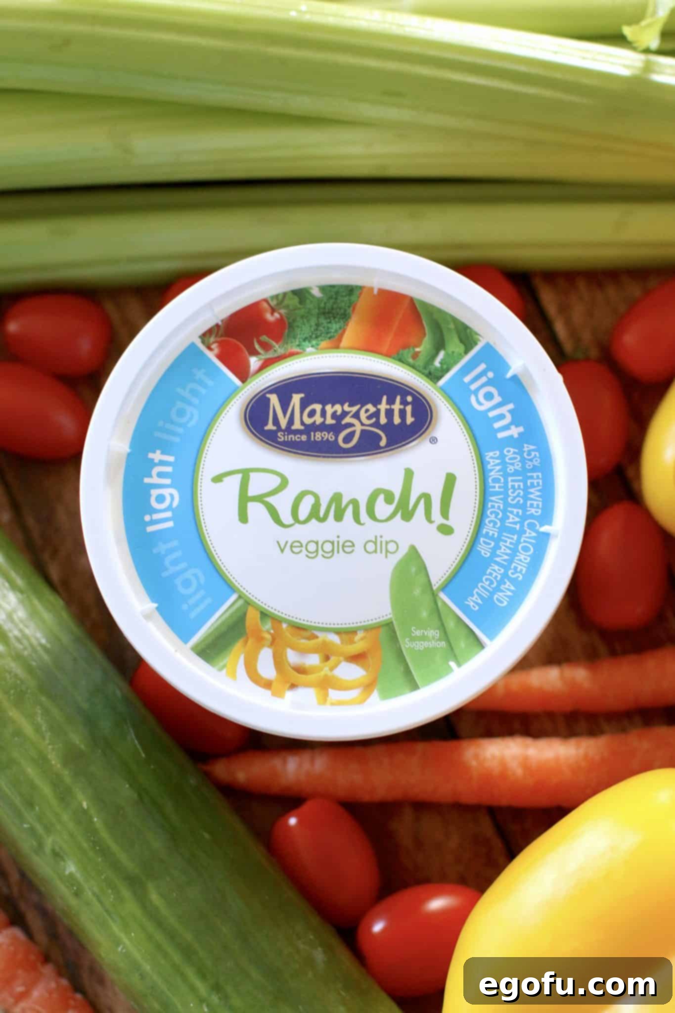 A tub of creamy ranch dressing surrounded by an assortment of fresh, colorful vegetables.