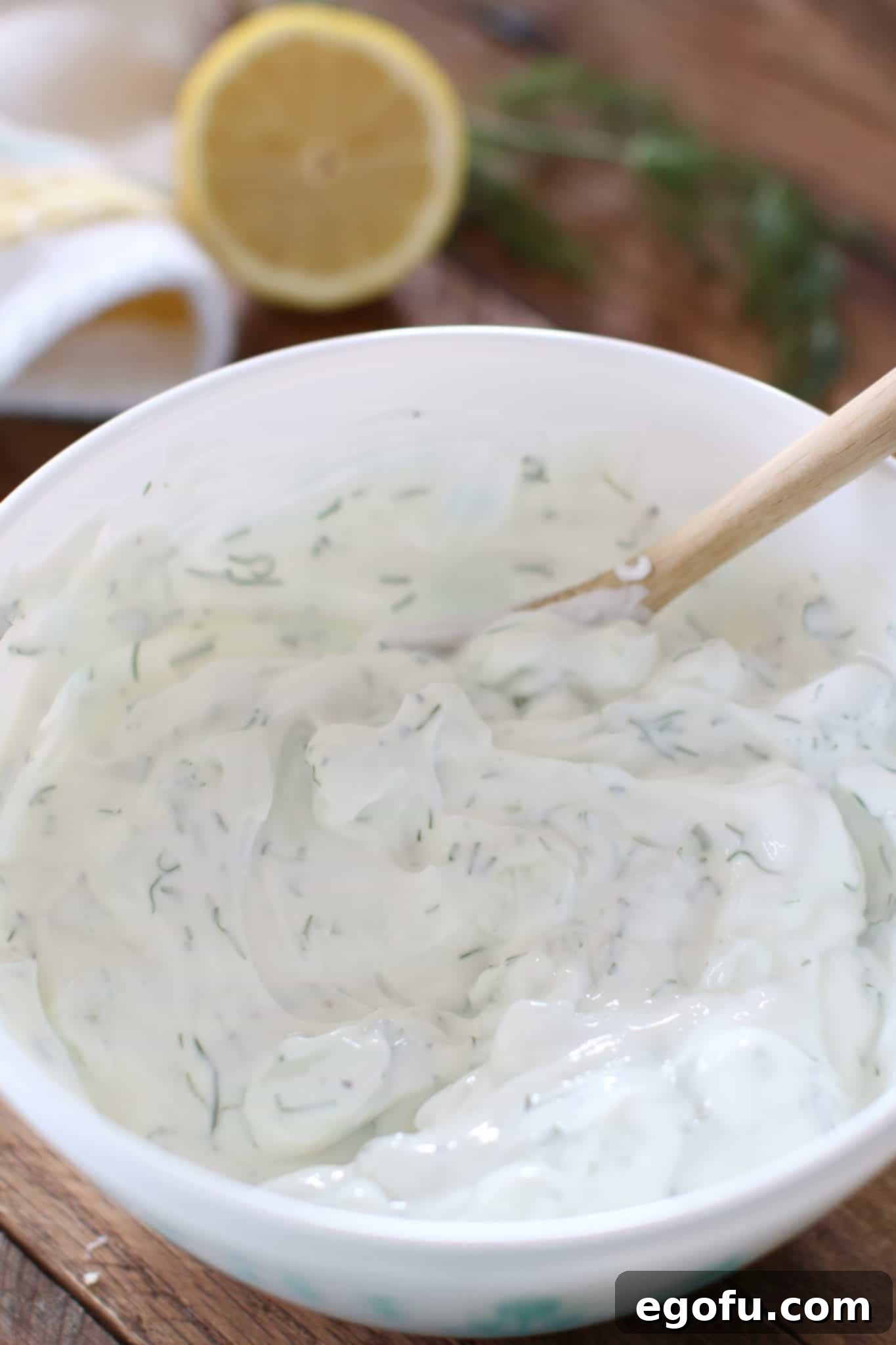 Tzatziki sauce stirred in a white bowl with a small wooden spoon.