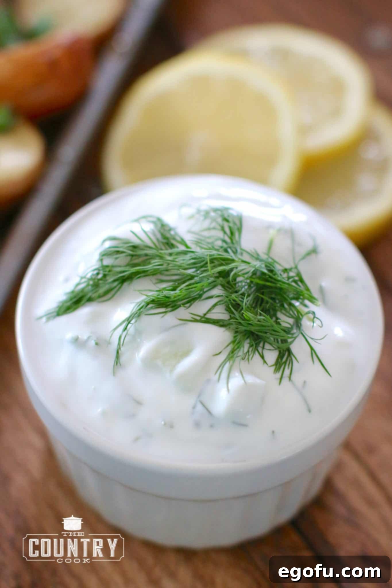 Tzatziki Sauce shown in a small white serving bowl with fresh dill laid on top.