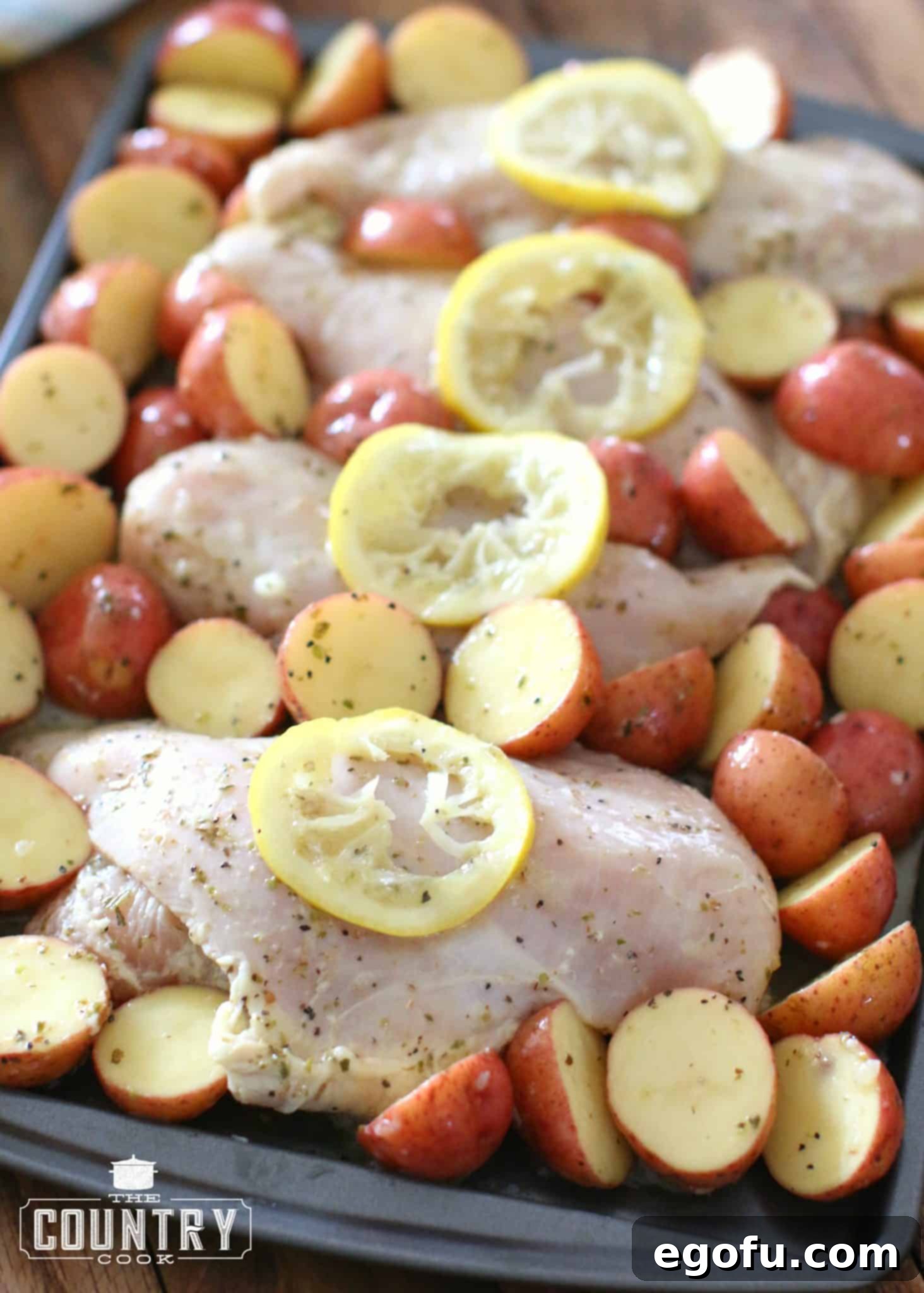 Marinated chicken breasts and sliced little potatoes placed evenly on a baking sheet and topped with sliced lemon.