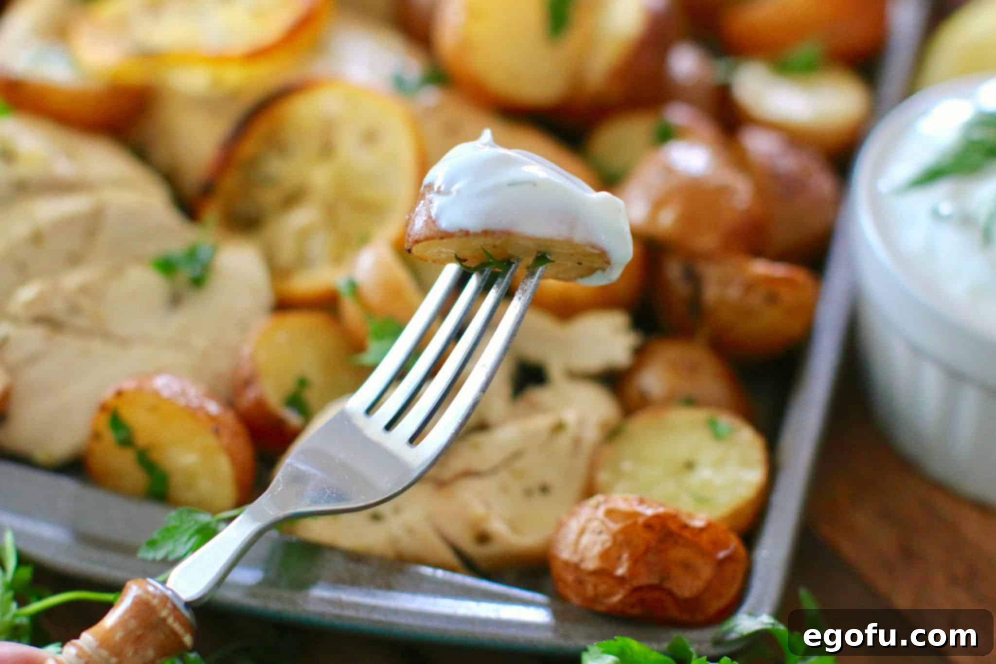 Fork holding half of a baked potato that has been dipped in tzatziki sauce.