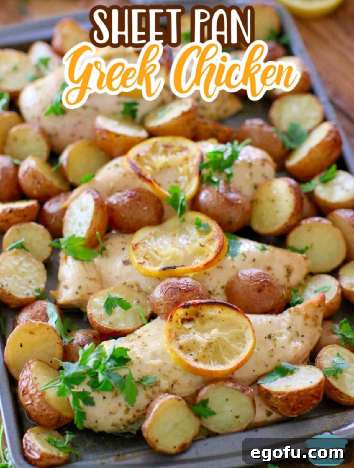 A sheet pan with cooked Greek chicken topped with lemon slices and cooked sliced potatoes.