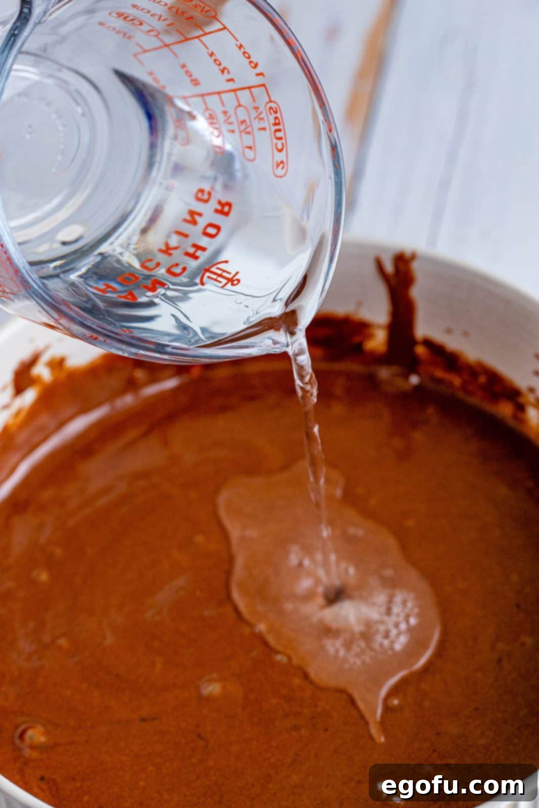 hot water added to chocolate cake batter in a white bowl.