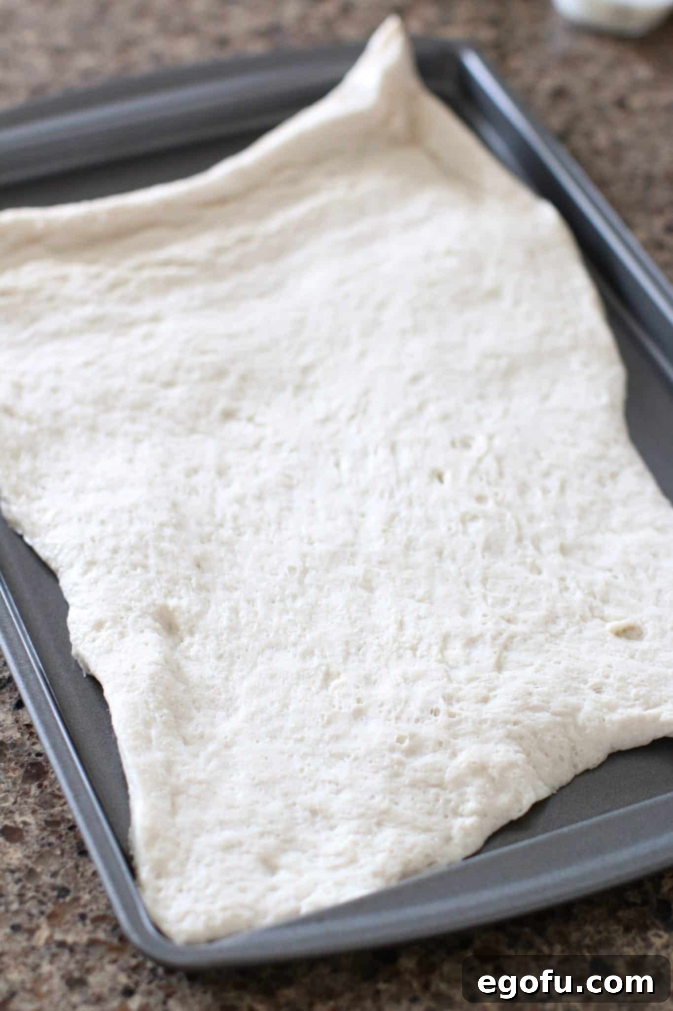 Refrigerated pizza dough unrolled and laid out on a baking sheet, ready for the oven.