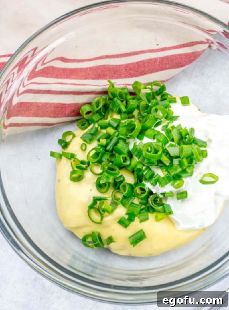 Sour cream, cream of chicken soup, and sliced green onion are mixed in a glass bowl, creating the creamy base for the casserole.