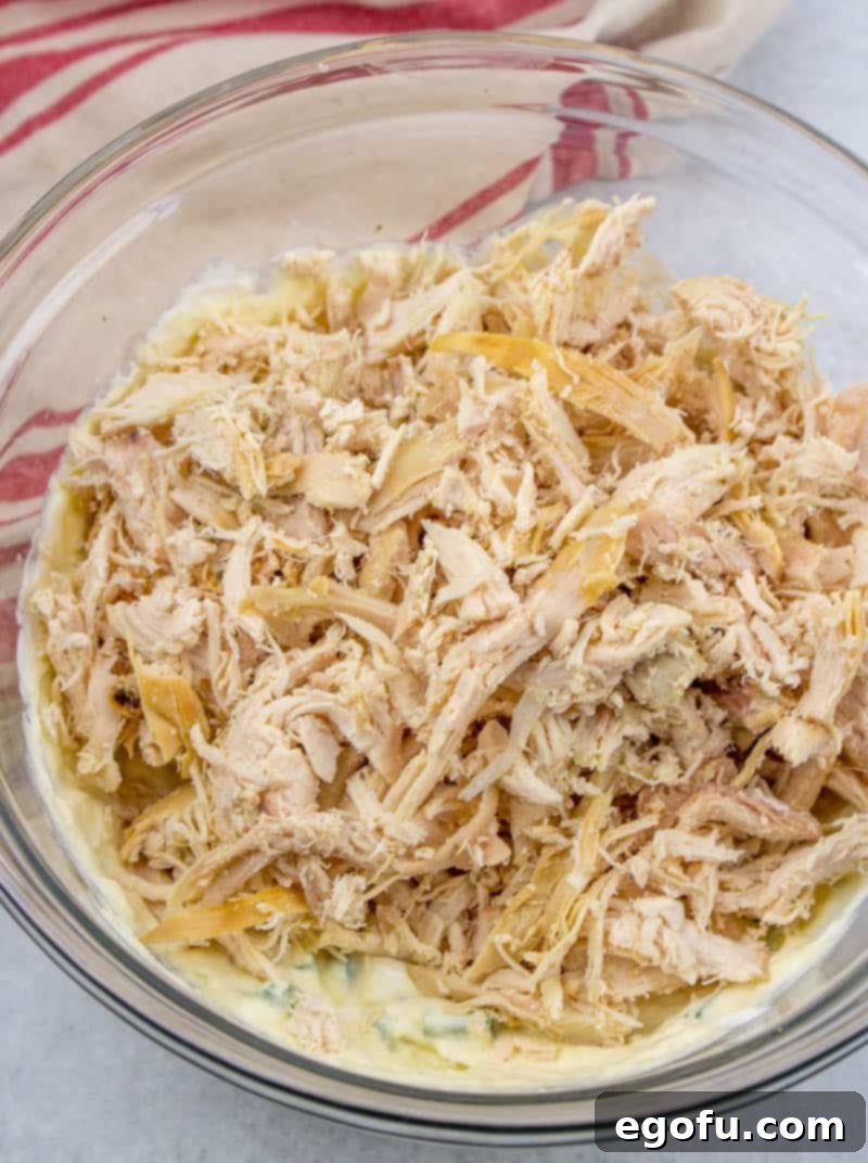 Shredded cooked chicken is mixed thoroughly with the creamy soup, sour cream, and green onion mixture in a bowl.