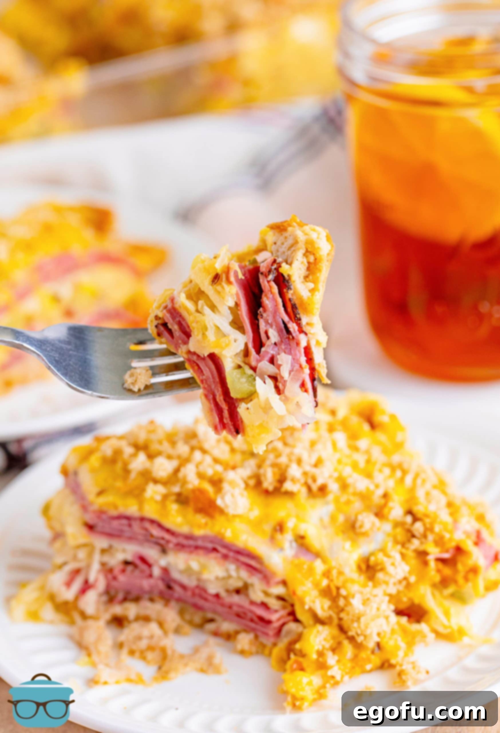 A fork holding a bite of Reuben Casserole above a plate with a serving of it.