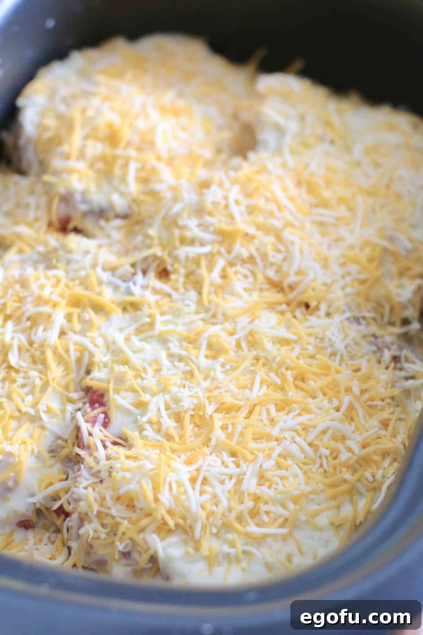 Slow cooker filled with layered pork chops, potatoes, sauce, and cheese before cooking