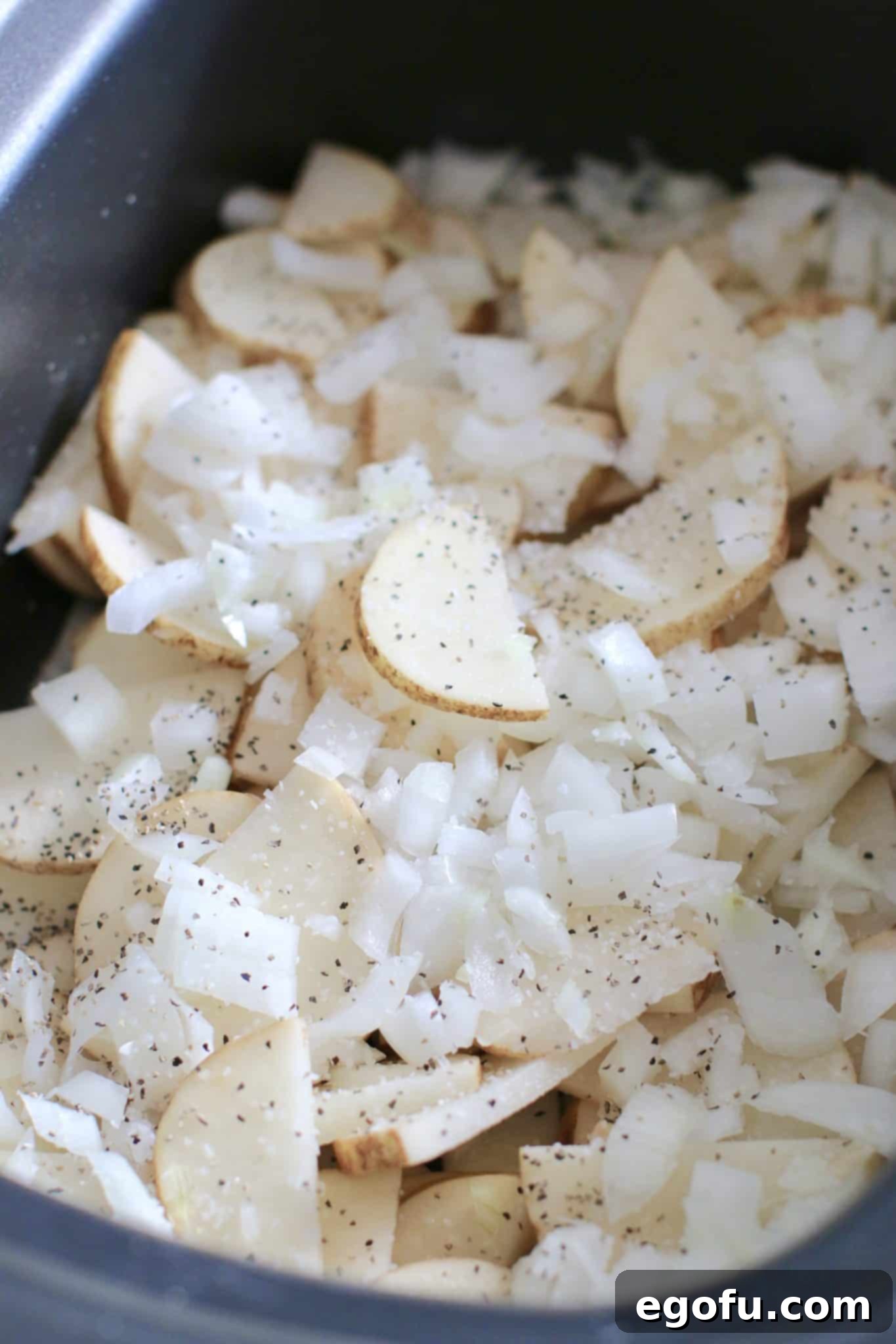 Potatoes and onions layered at the bottom of a slow cooker for Smothered Pork Chops