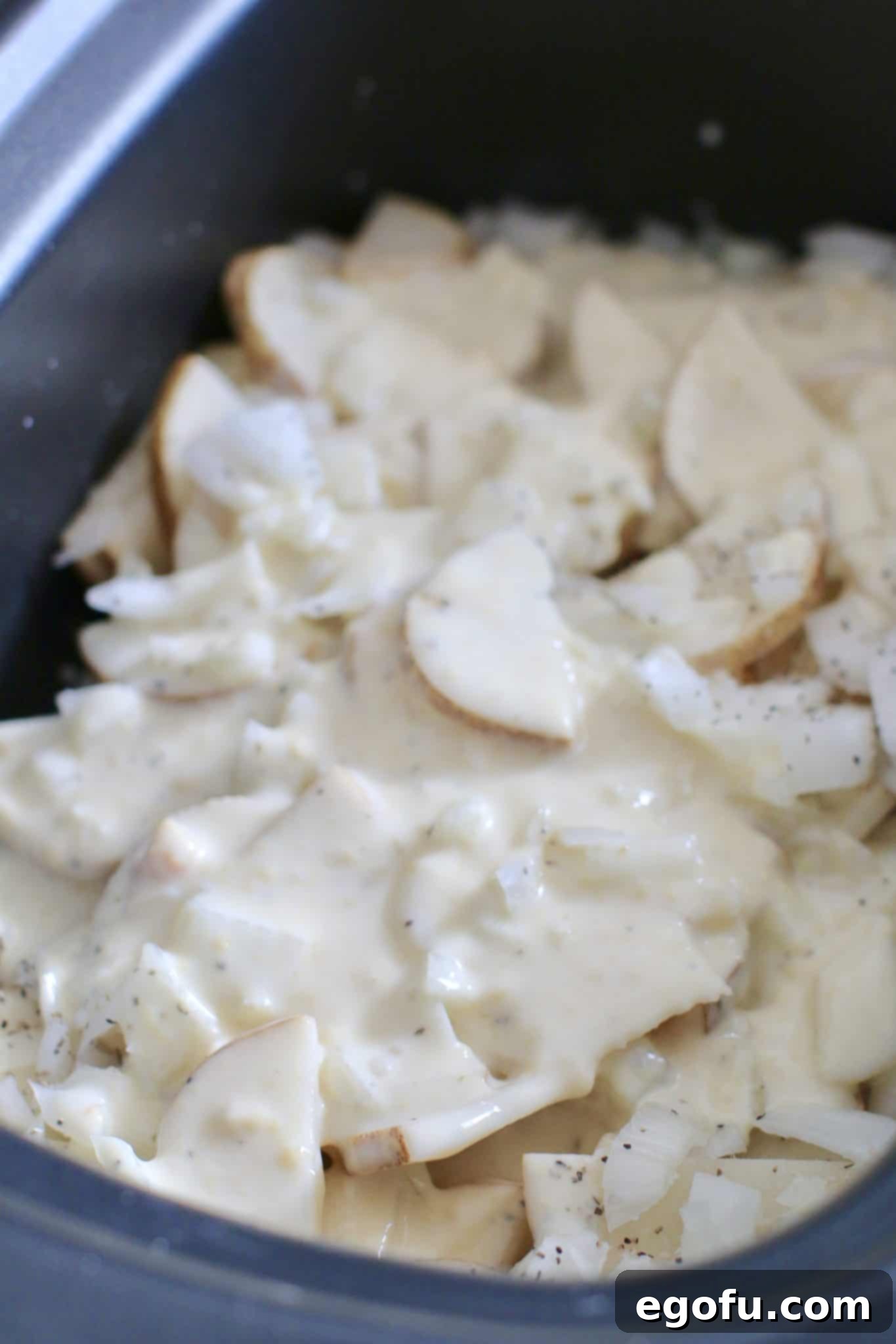 Half of the sauce mixture spread over potatoes in the slow cooker for Smothered Pork Chops