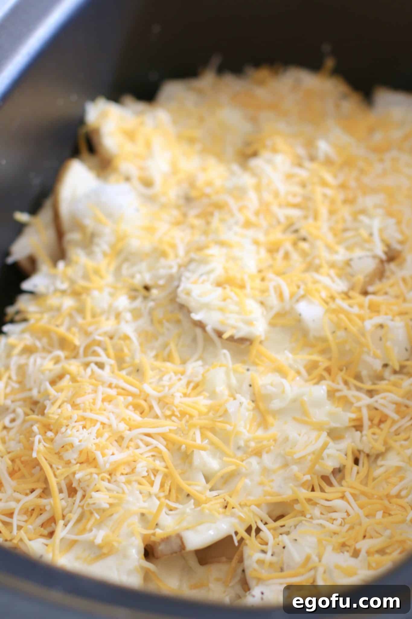 Cheese sprinkled over potatoes and sauce in the slow cooker for Smothered Pork Chops