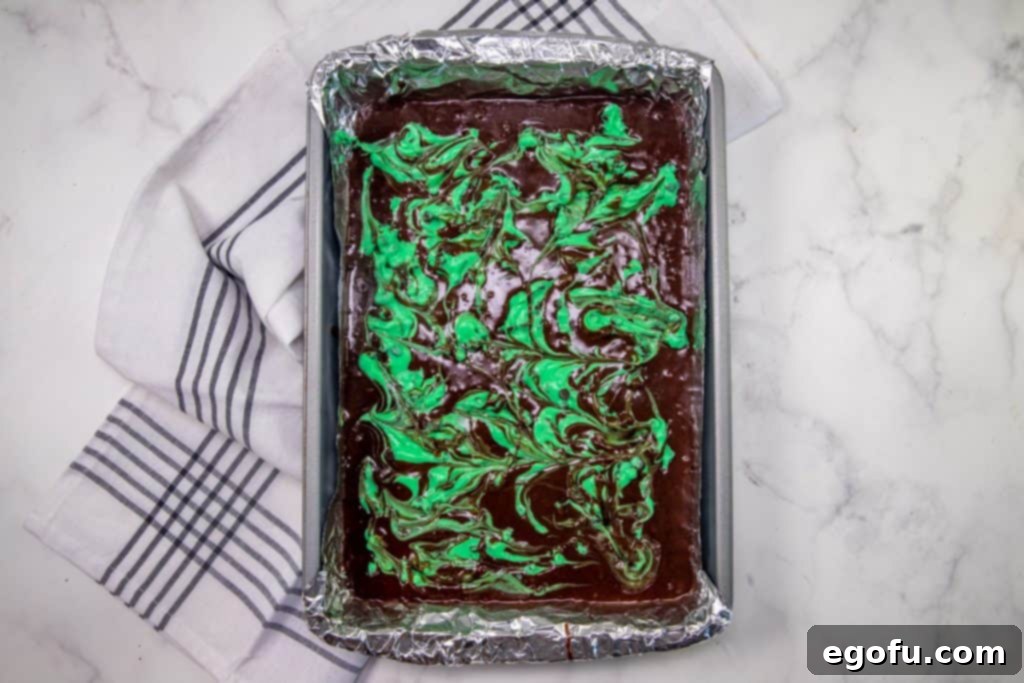 green cream cheese shown swirled through brownie batter in baking pan