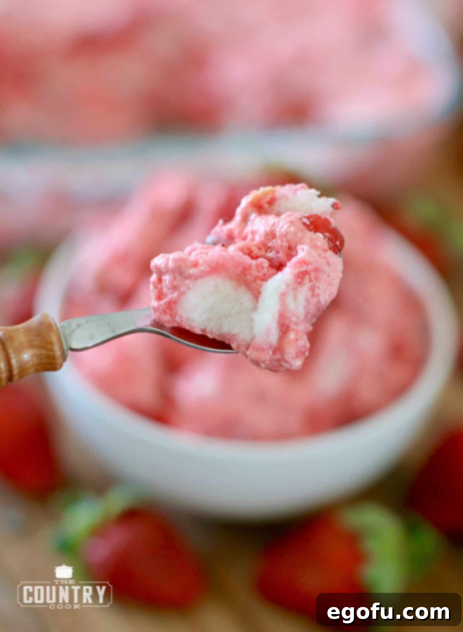Strawberry Angel Delight 13 A wooden spoon holding up a perfectly portioned bite of no-bake strawberry angel dessert, showing its appealing texture and layers.