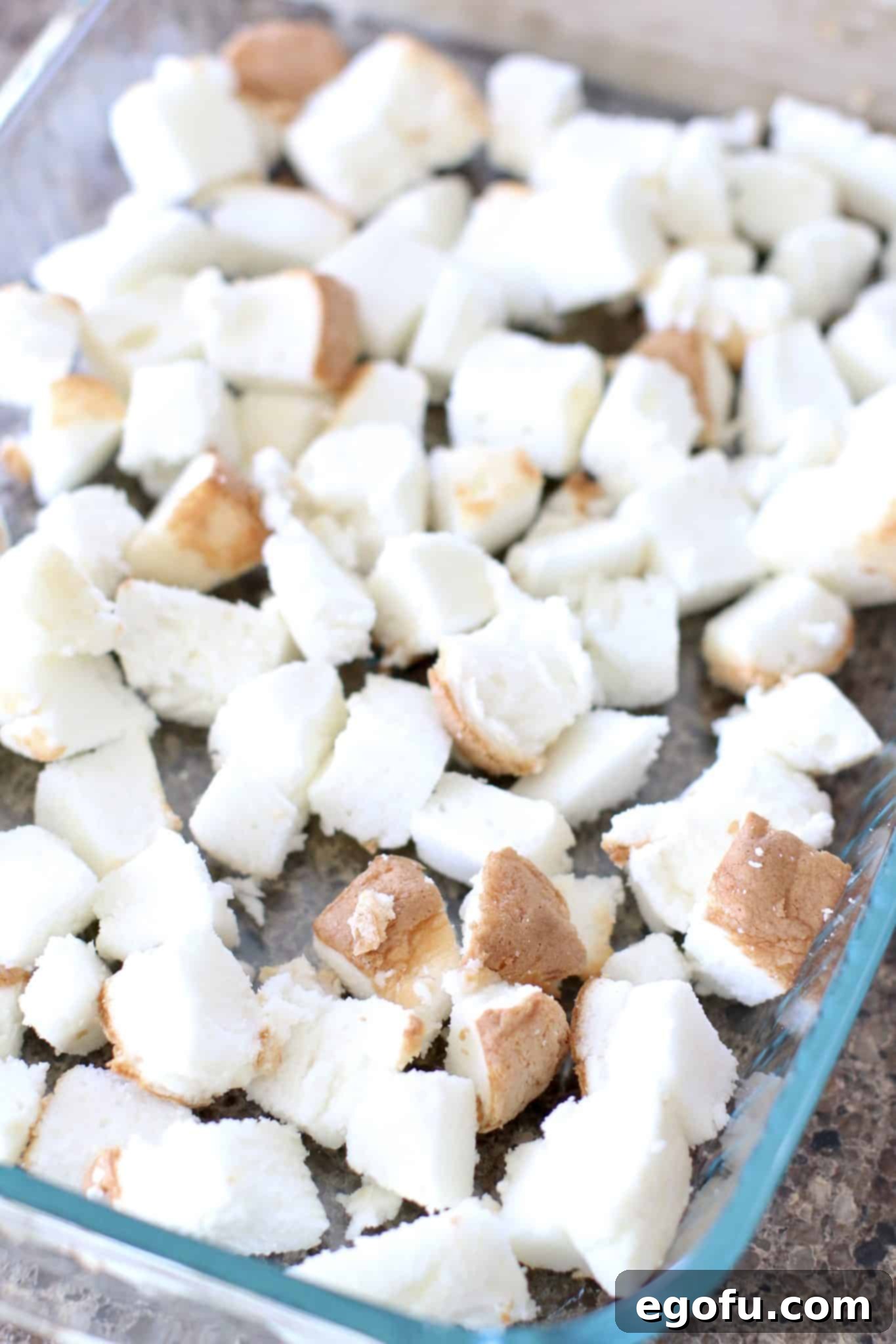 Strawberry Angel Delight 6 Diced angel food cake pieces forming an even layer at the bottom of a clear glass baking dish.
