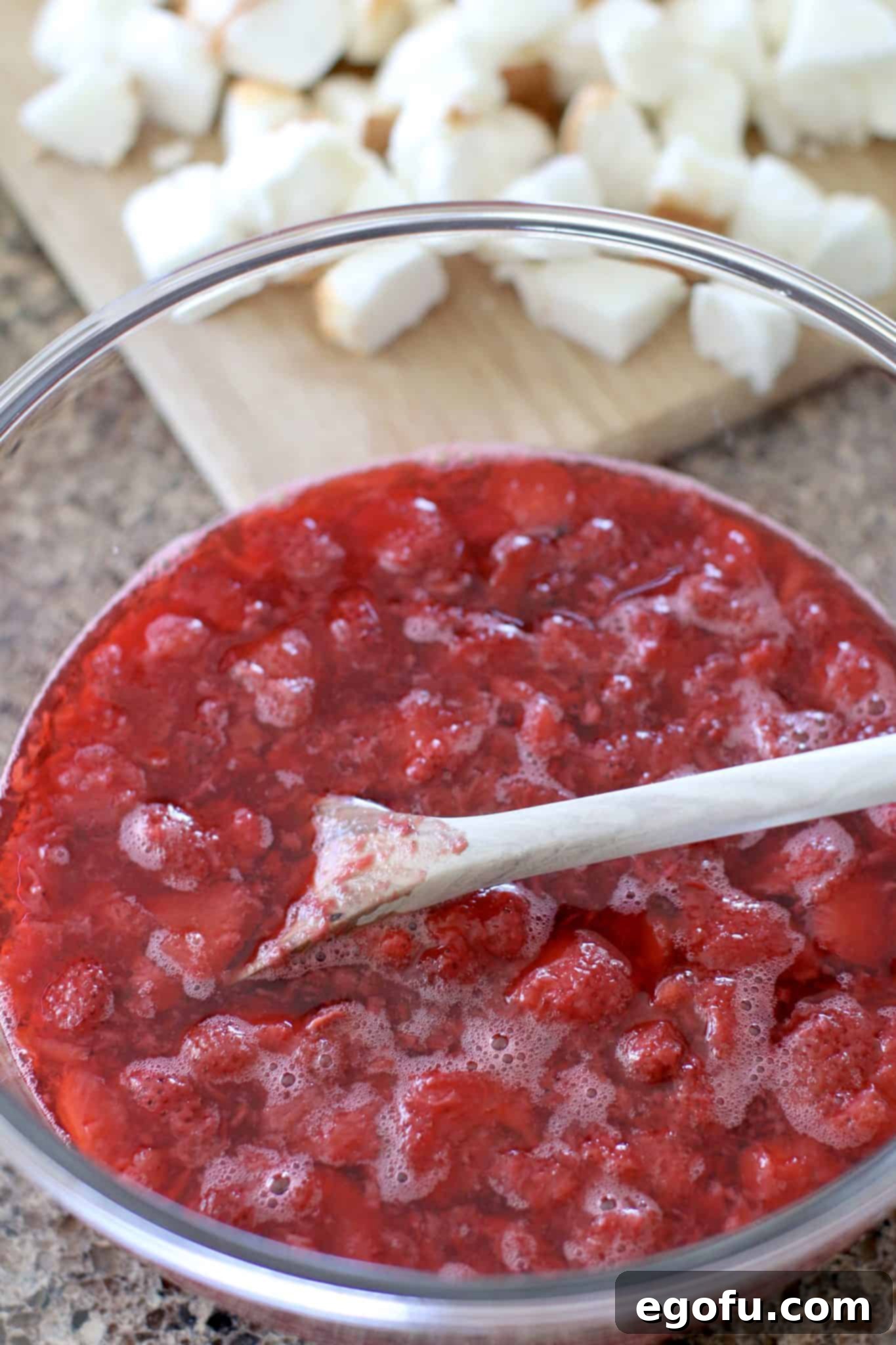 Strawberry Angel Delight 8 Thawed frozen strawberries mixed into the vibrant strawberry gelatin mixture in a glass mixing bowl.