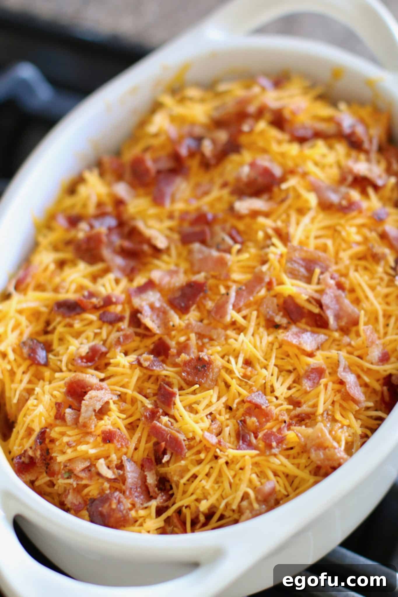 shredded cheese and chopped bacon shown covering the tex Mex potatoes in the white oval baking dish.