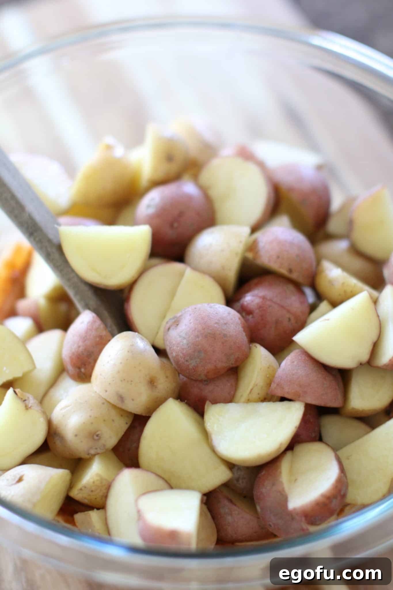 halved potatoes shown in a clear bowl with a wooden spoon.