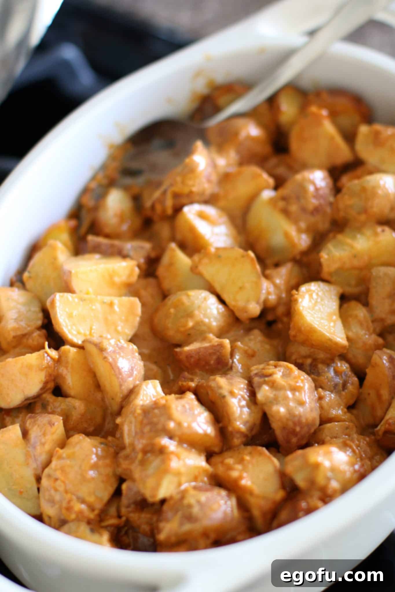 partially baked tex Mex potatoes shown in a white oval baking dish with a silver spoon.