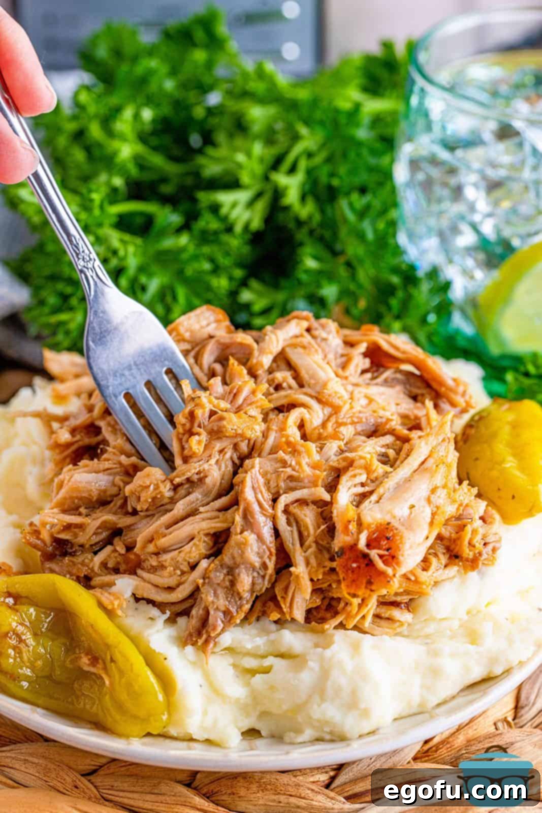 Fall-Apart Mississippi Pork Perfection 2 A fork shown inside shredded pork that is on top of mashed potatoes on a plate, highlighting the tenderness and appetizing presentation.