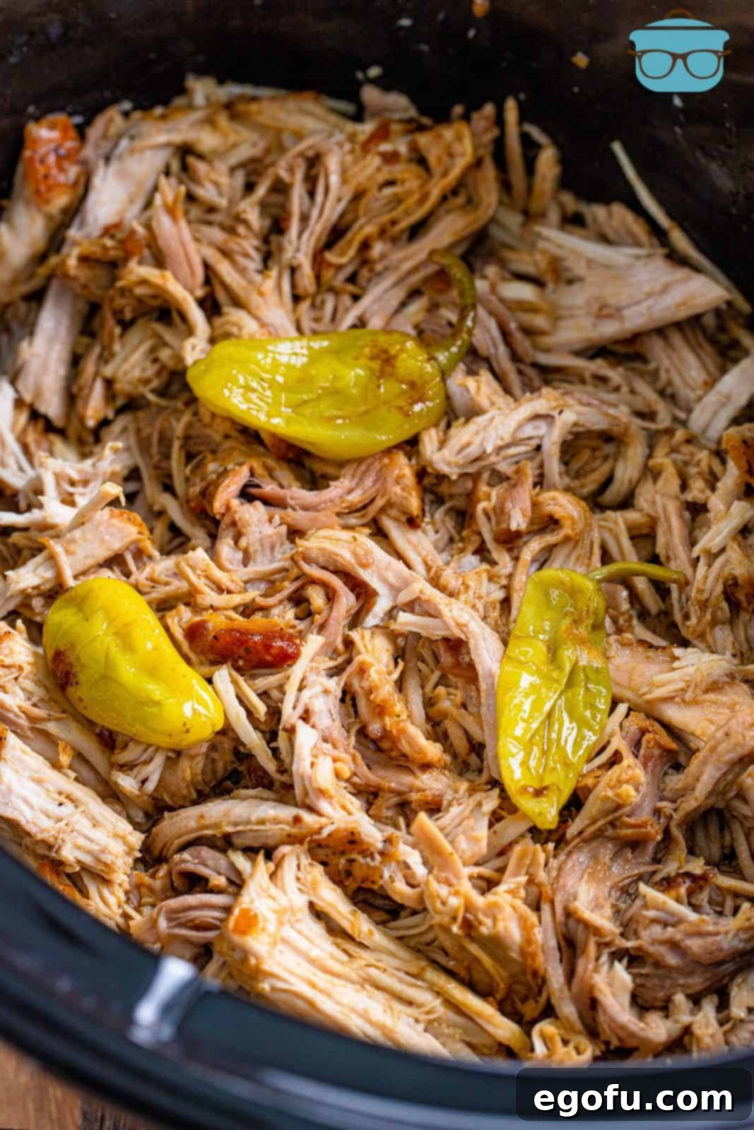 Fall-Apart Mississippi Pork Perfection 12 Fully cooked and shredded pork roast topped with pepperoncini peppers in a slow cooker, ready to be served.