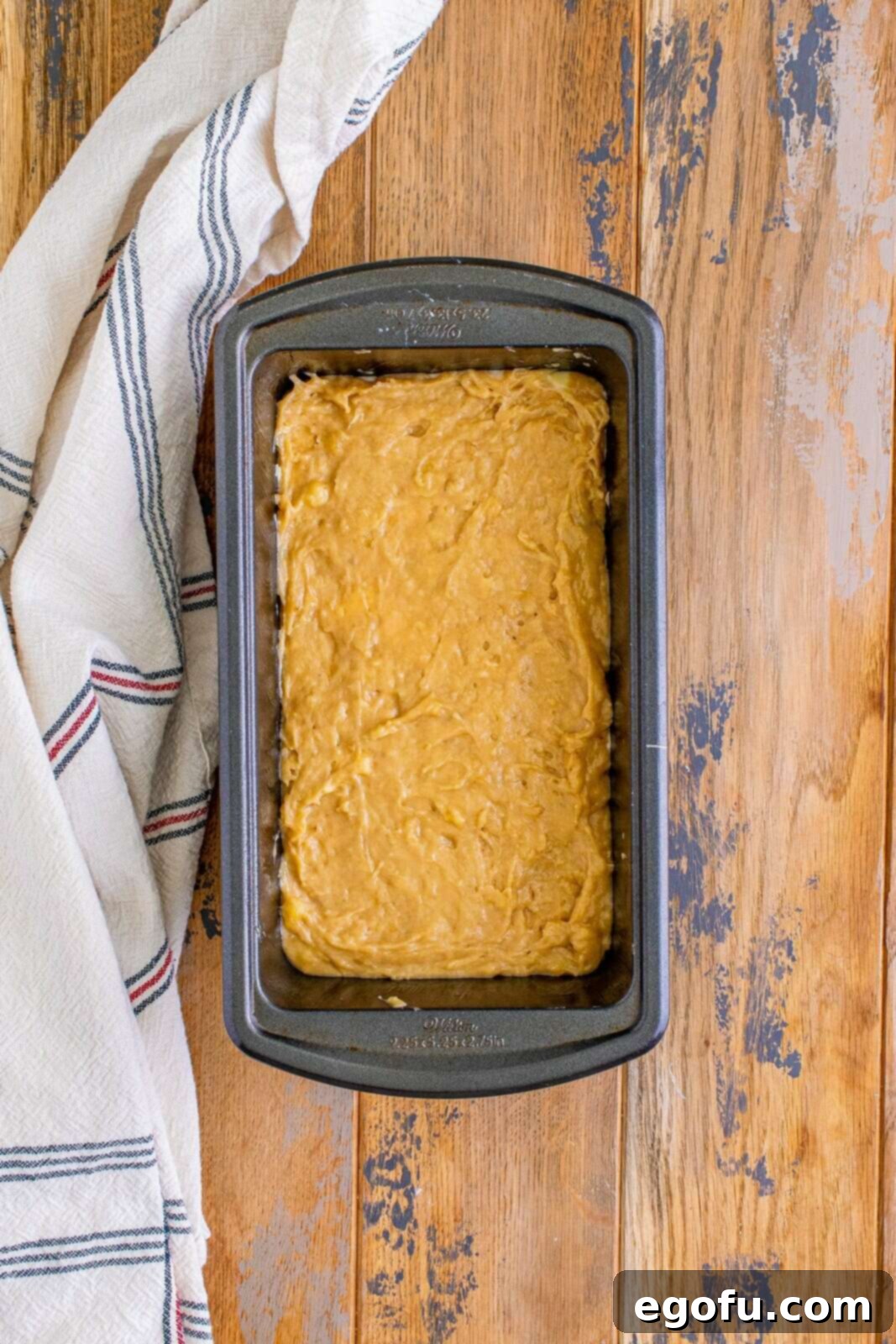 Cream Cheese Swirl Banana Bread 12 The final layer of banana bread batter being added onto the cheesecake layer in the loaf pan, completing the assembly.
