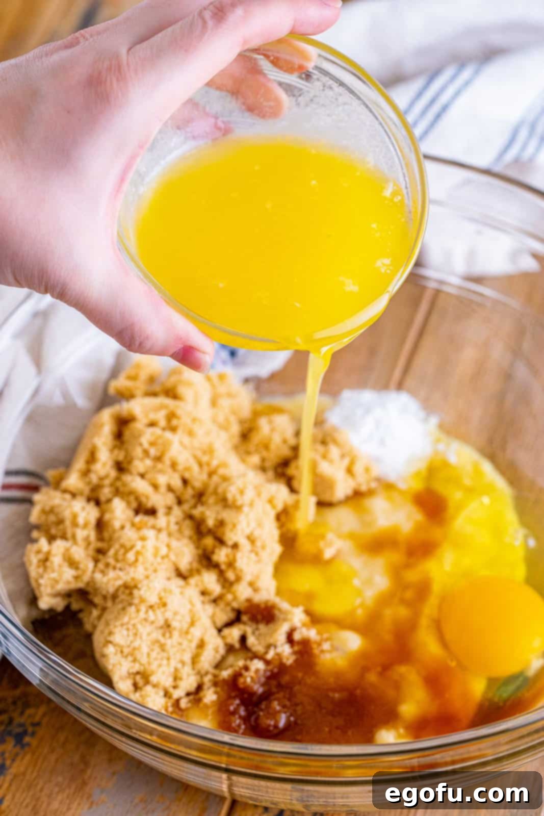 Cream Cheese Swirl Banana Bread 5 A small bowl of melted butter being poured into a larger bowl with mashed bananas, sugar, egg, vanilla, and baking soda, combining ingredients for the banana bread batter.