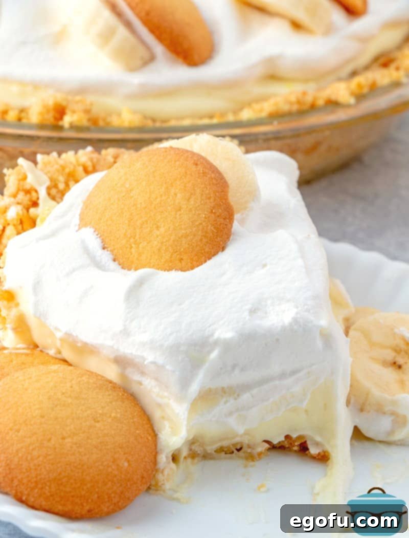 A delectable slice of New York Banana Cream Pie on a plate, showcasing its layered homemade Nilla wafer crust, creamy banana filling, and whipped topping.