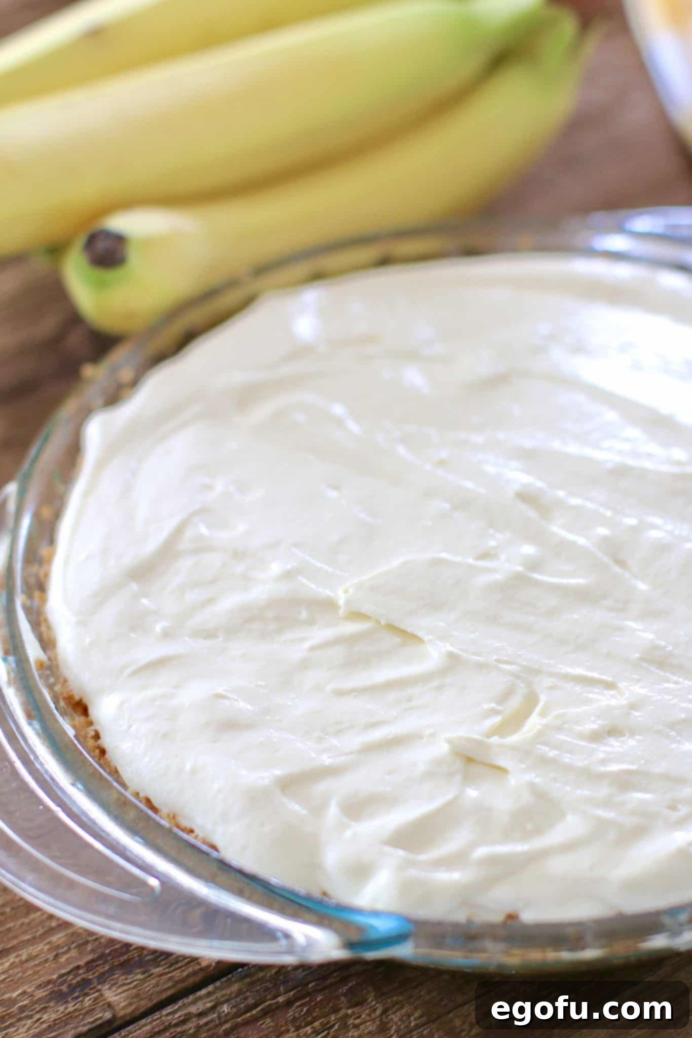 Banana cream pie filling poured smoothly over the banana slices in the crust, creating a luscious layer.