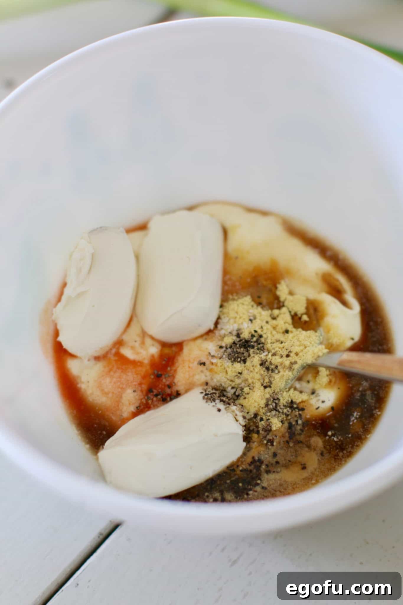 A creamy mixture of cream cheese, mayonnaise, Worcestershire sauce, apple cider vinegar, hot sauce, sugar, dried mustard, salt, and pepper in a white mixing bowl, ready for the next ingredients.