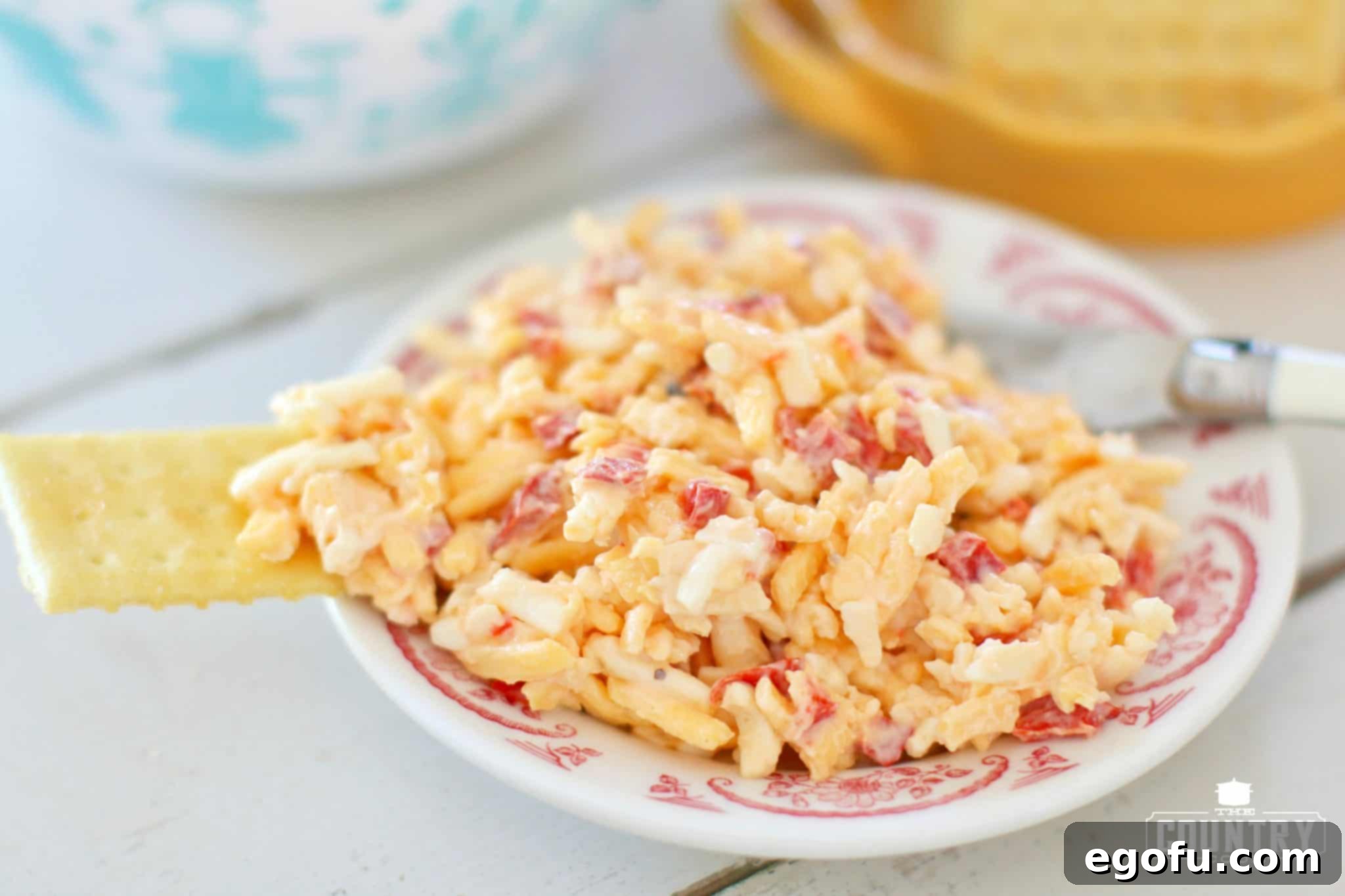 A single serving of pimento cheese on a small round white and red plate, accompanied by a club cracker, ready for a delightful snack.