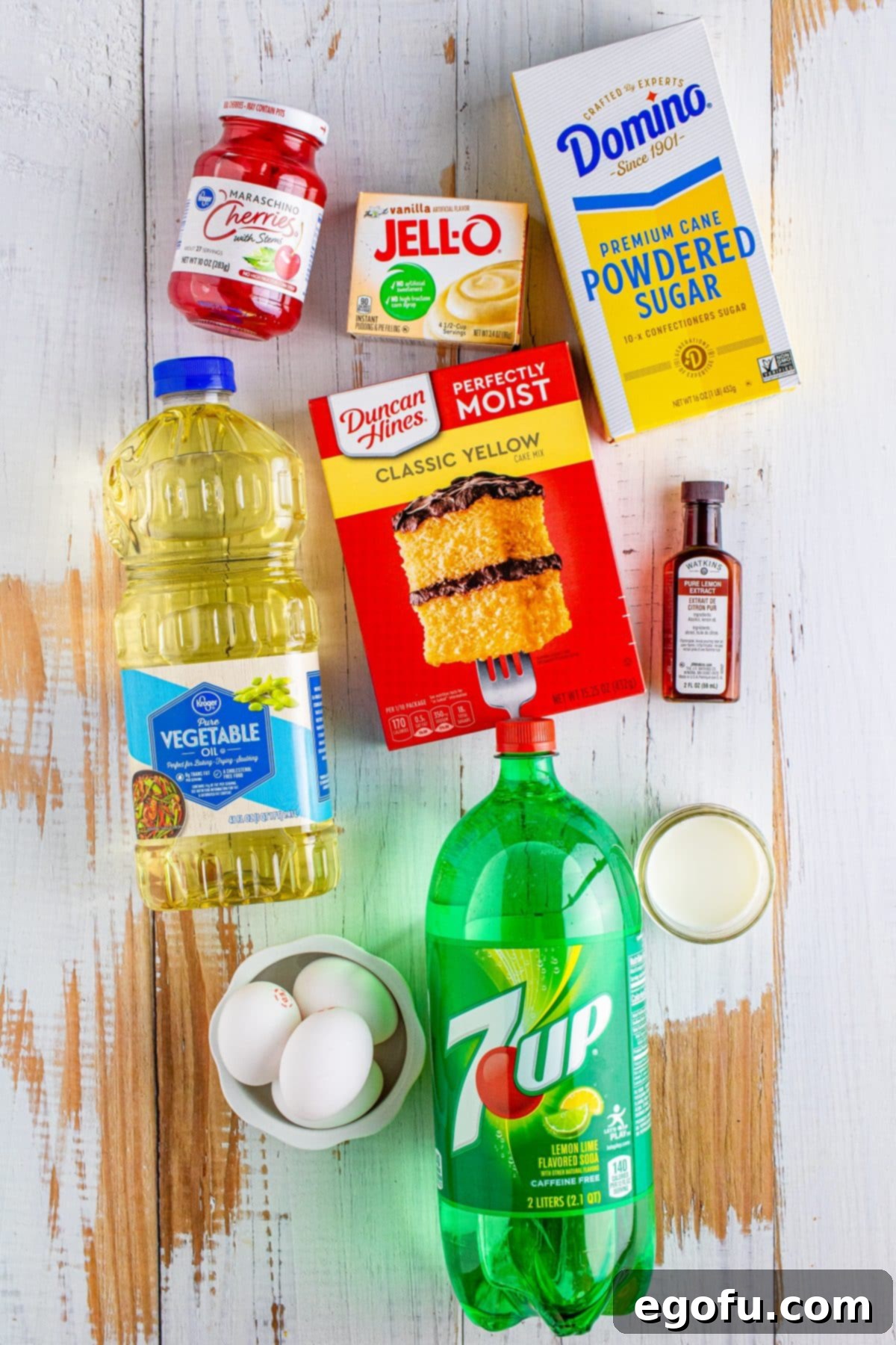 All ingredients laid out: yellow cake mix, vegetable oil, 7 Up, lemon extract, maraschino cherries, instant vanilla pudding mix, eggs, and powdered sugar, ready for baking.