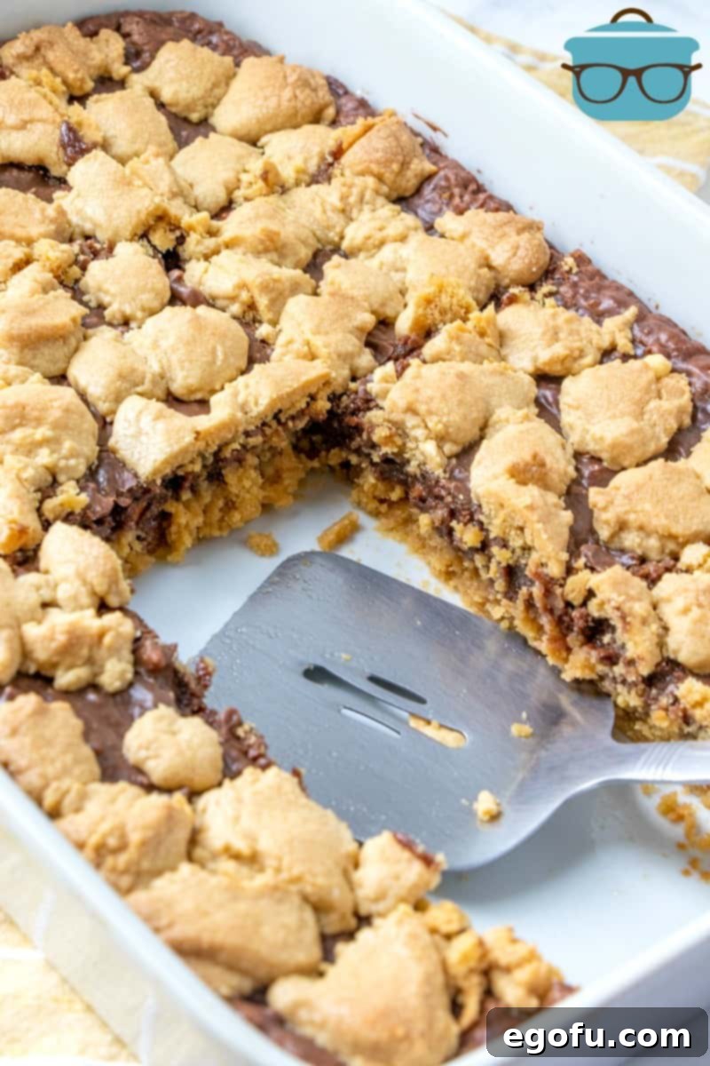 Fudge-filled Peanut Butter Bars in a baking dish, slices cut out and shown with a spatula.