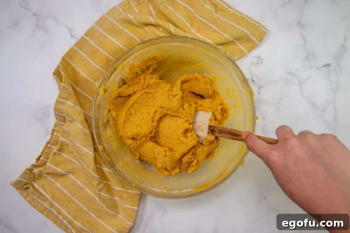 peanut butter, butter and eggs mixed together in a bowl with a rubber spatula. 