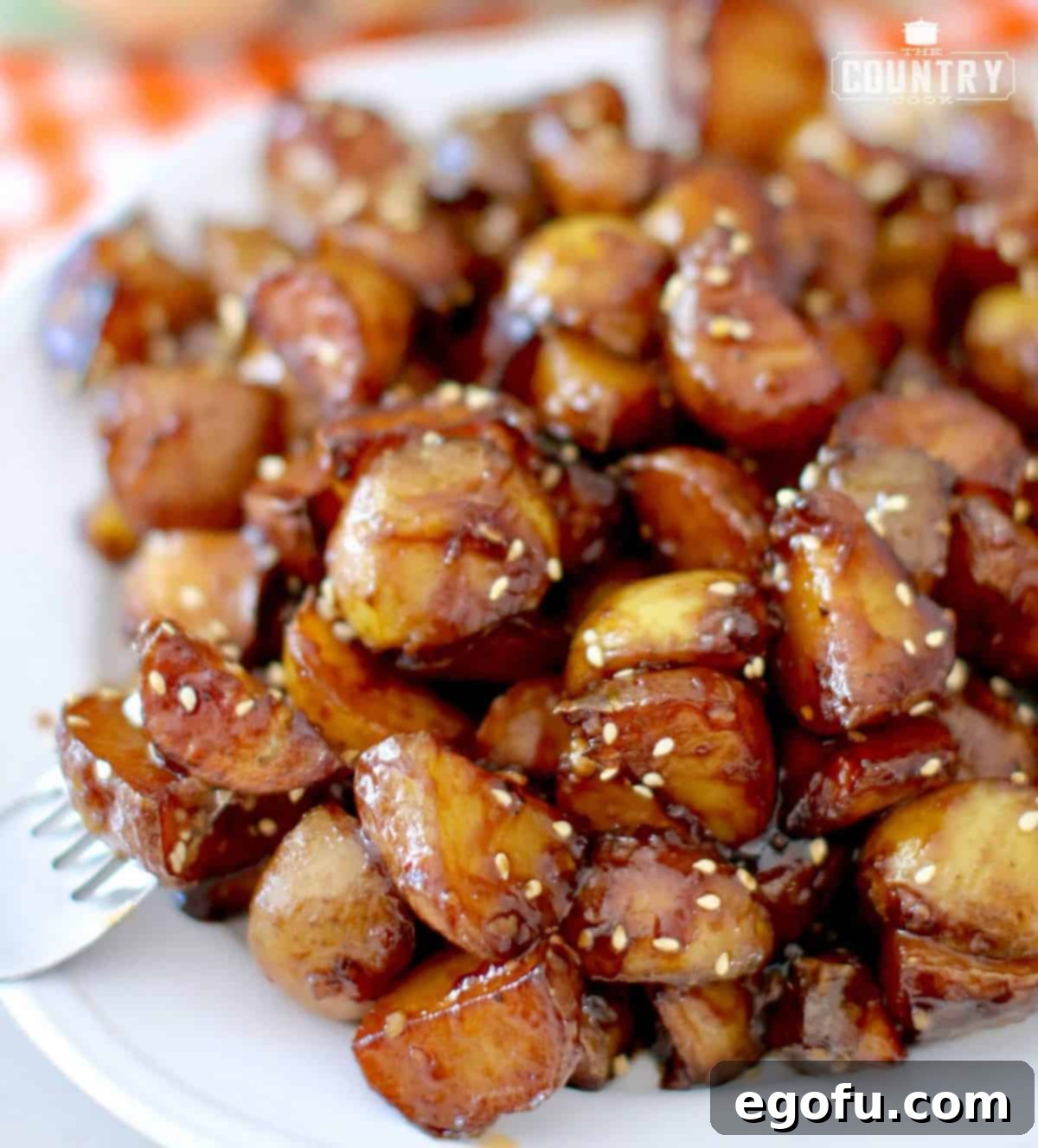 Sticky Potatoes topped with sesame seeds shown on a round white plate.