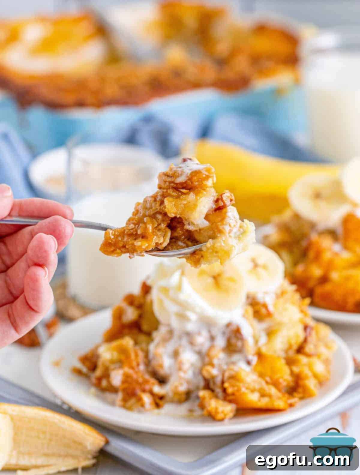 A close-up shot of a scoop of golden-brown Southern Banana Cobbler, showcasing its thick banana filling and crunchy pecan streusel topping, served on a white plate with fresh banana slices.