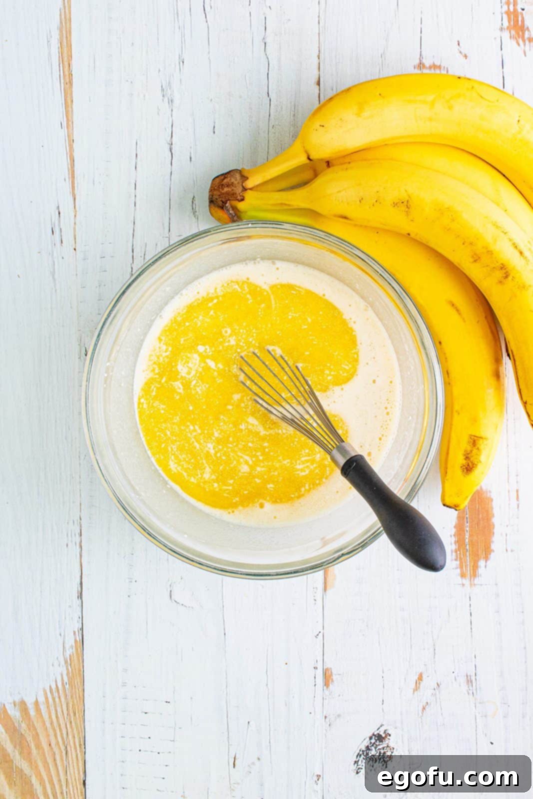 A bowl containing a smooth, creamy mixture of self-rising flour, granulated sugar, milk, and melted butter, whisked together to form the rich cobbler filling.