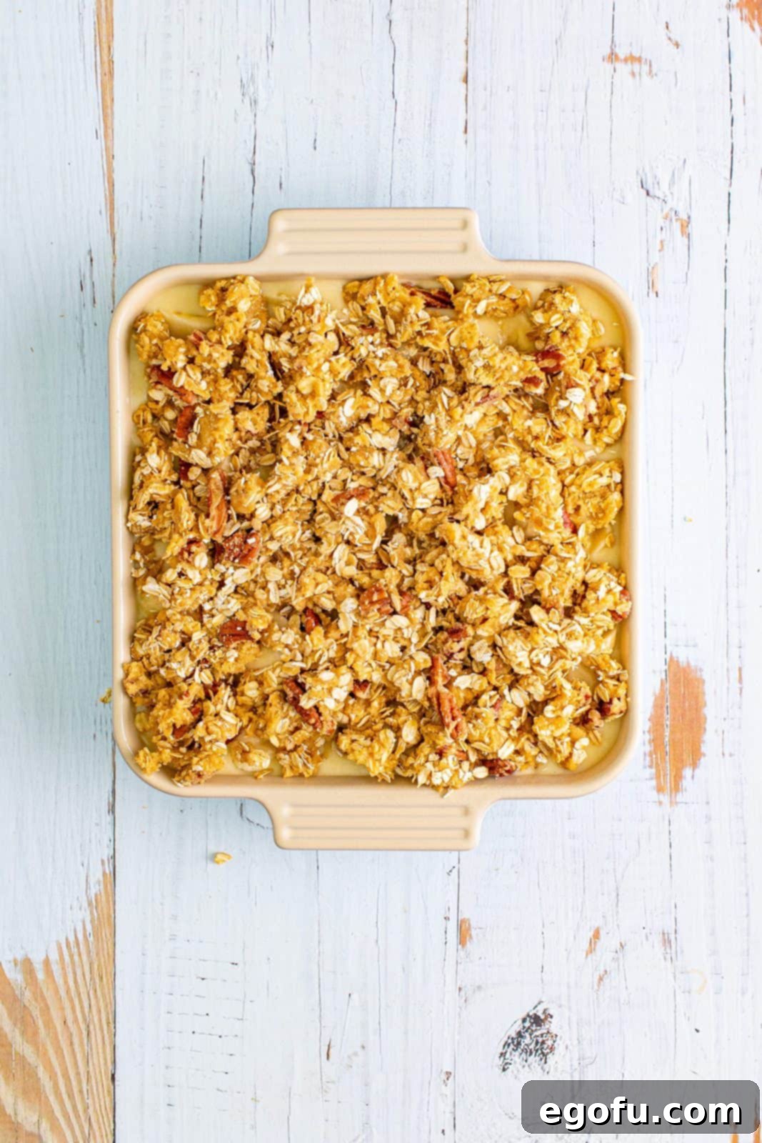 The delicious crumbly streusel topping, made with oats and pecans, is generously spread over the layer of sliced bananas in the baking dish, creating a textural contrast for the cobbler.