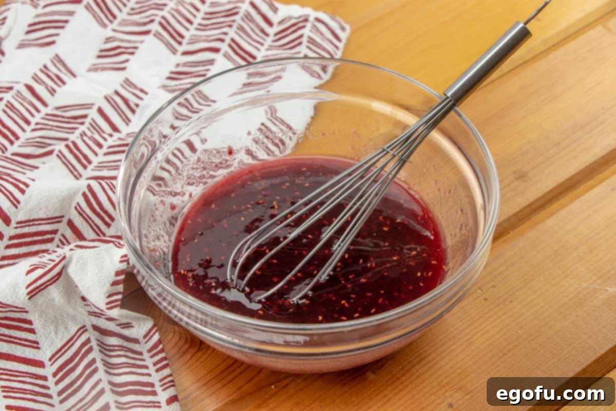whisking together raspberry preserves with water in a clear bowl.