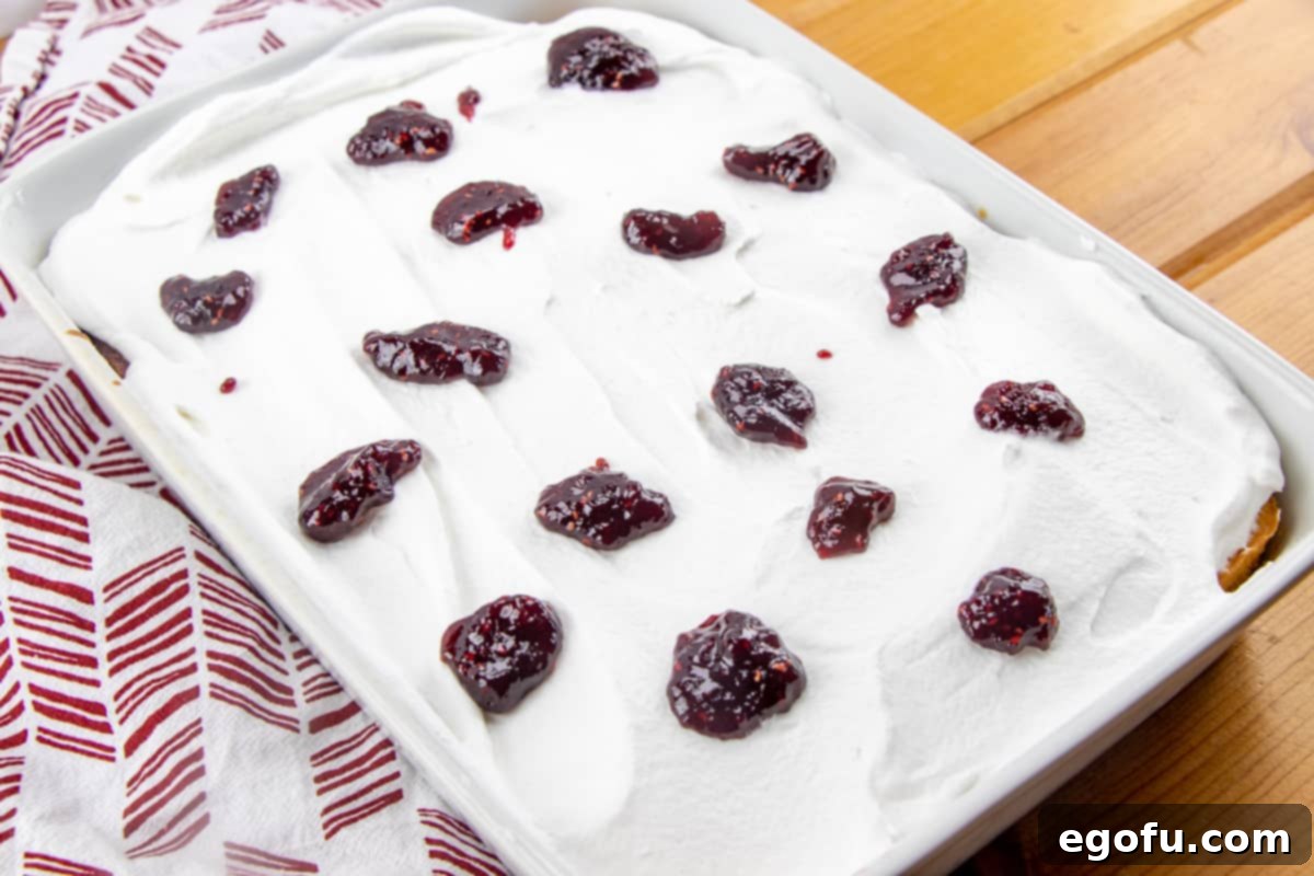 raspberry preserves dolloped on whipped cream on top of lemon cake.