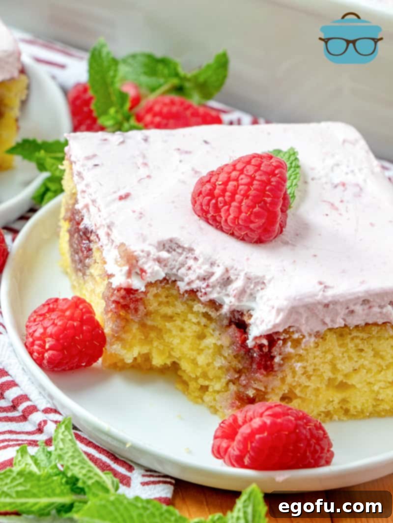 slice of Lemon Raspberry Poke Cake on a white plate with a bite cut out.