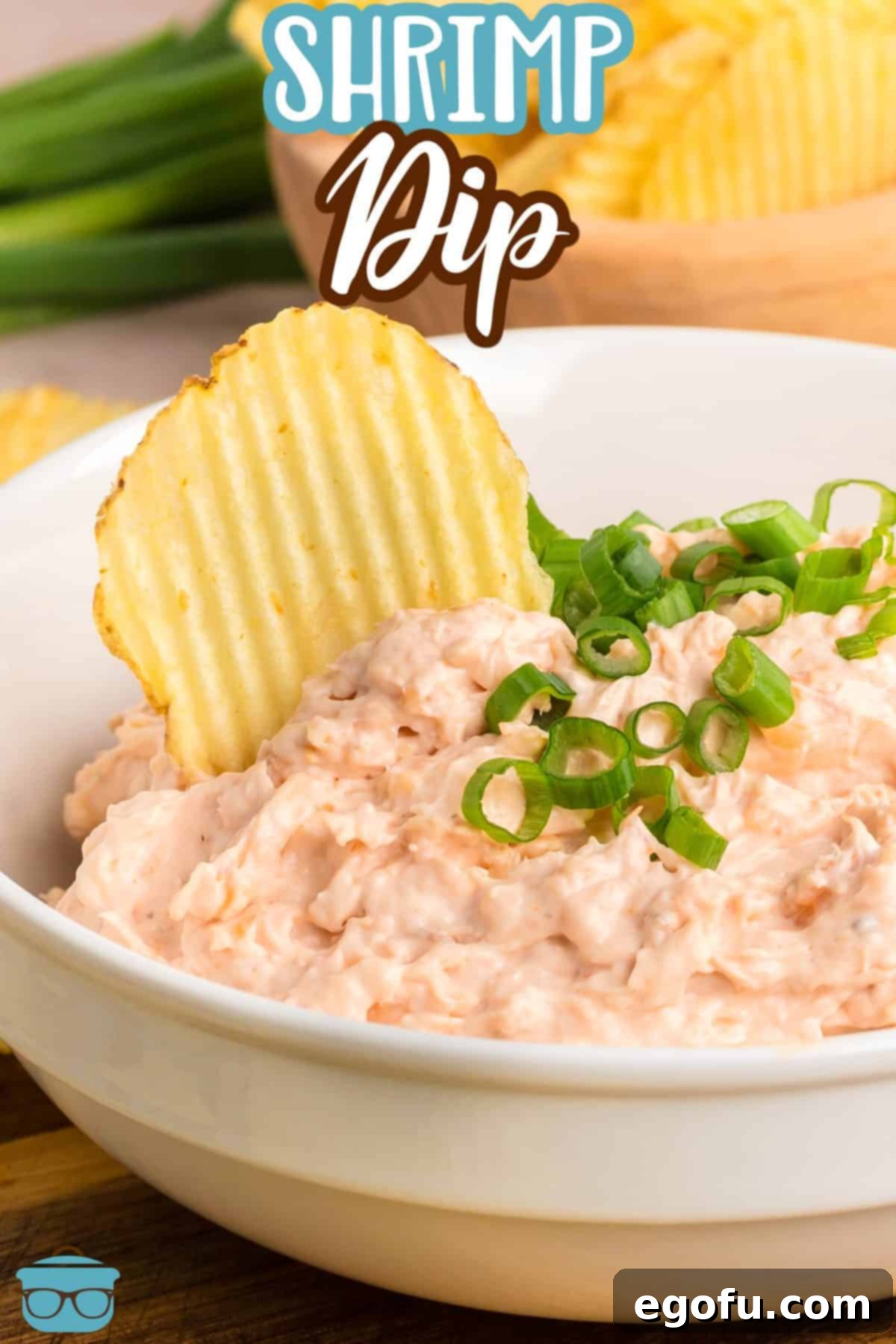 A small bowl of creamy Shrimp Dip with a crispy potato chip perfectly poised for dipping.