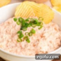 A close-up view of a bowl of creamy Shrimp Dip, with a potato chip poised, highlighting its inviting texture.