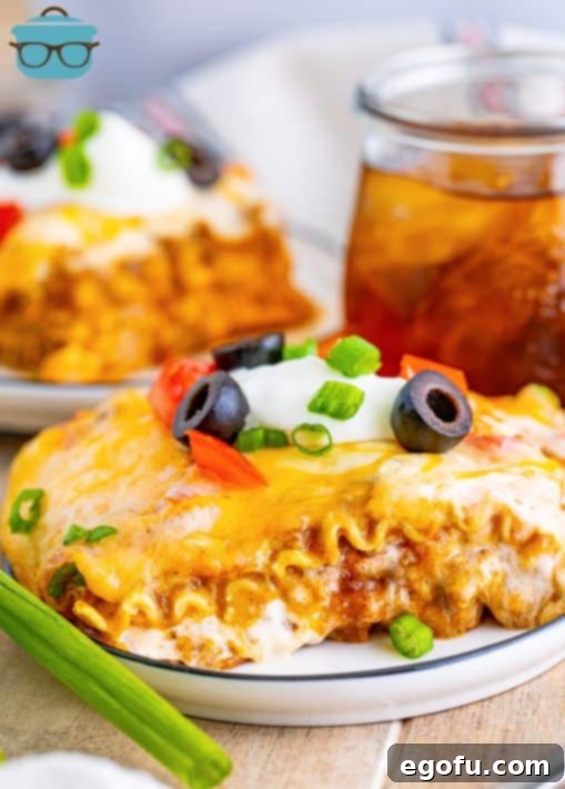 a slice of mexican lasagna on a white plate with iced tea in the background.