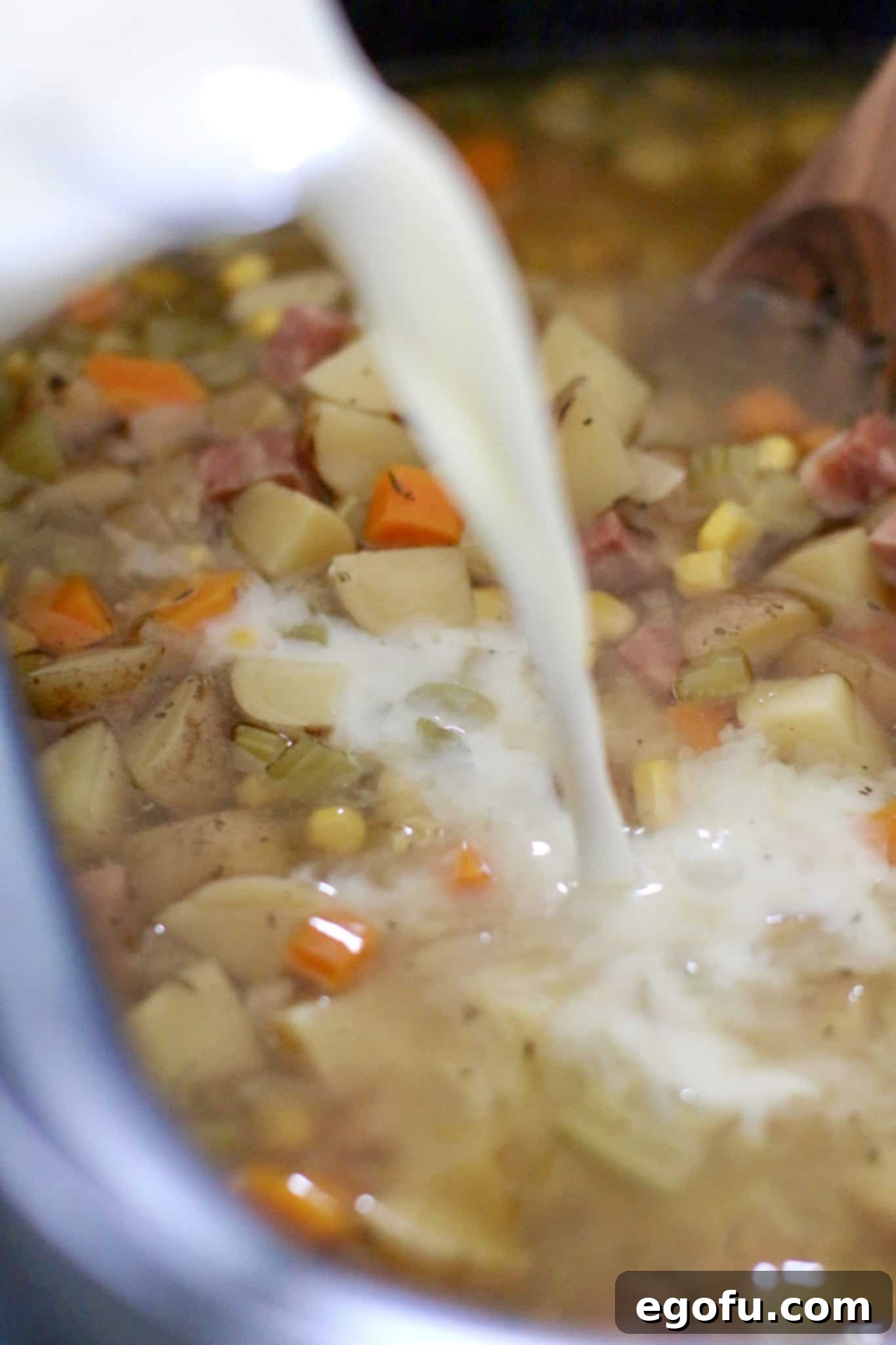 milk being poured into corn chowder in an oval slow cooker.