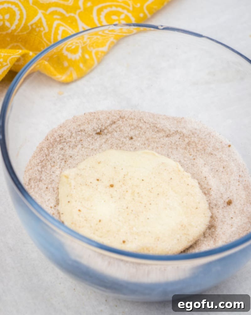 Coating biscuit slice with cinnamon sugar mixture in a bowl for pumpkin pull-apart bread