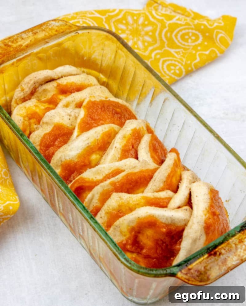 Stacked biscuits and pumpkin mixture arranged in a bread loaf pan, ready for baking